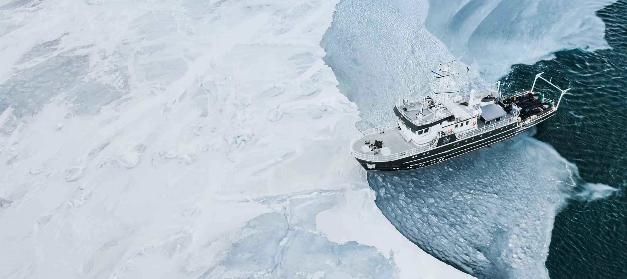 The R/V Kinfish at anchor in a still Arctic bay, a zodiac and drifting ice alongside
